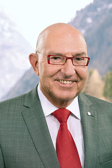 Friedrich P. Wackler in Anzug vor Berglandschaft.
