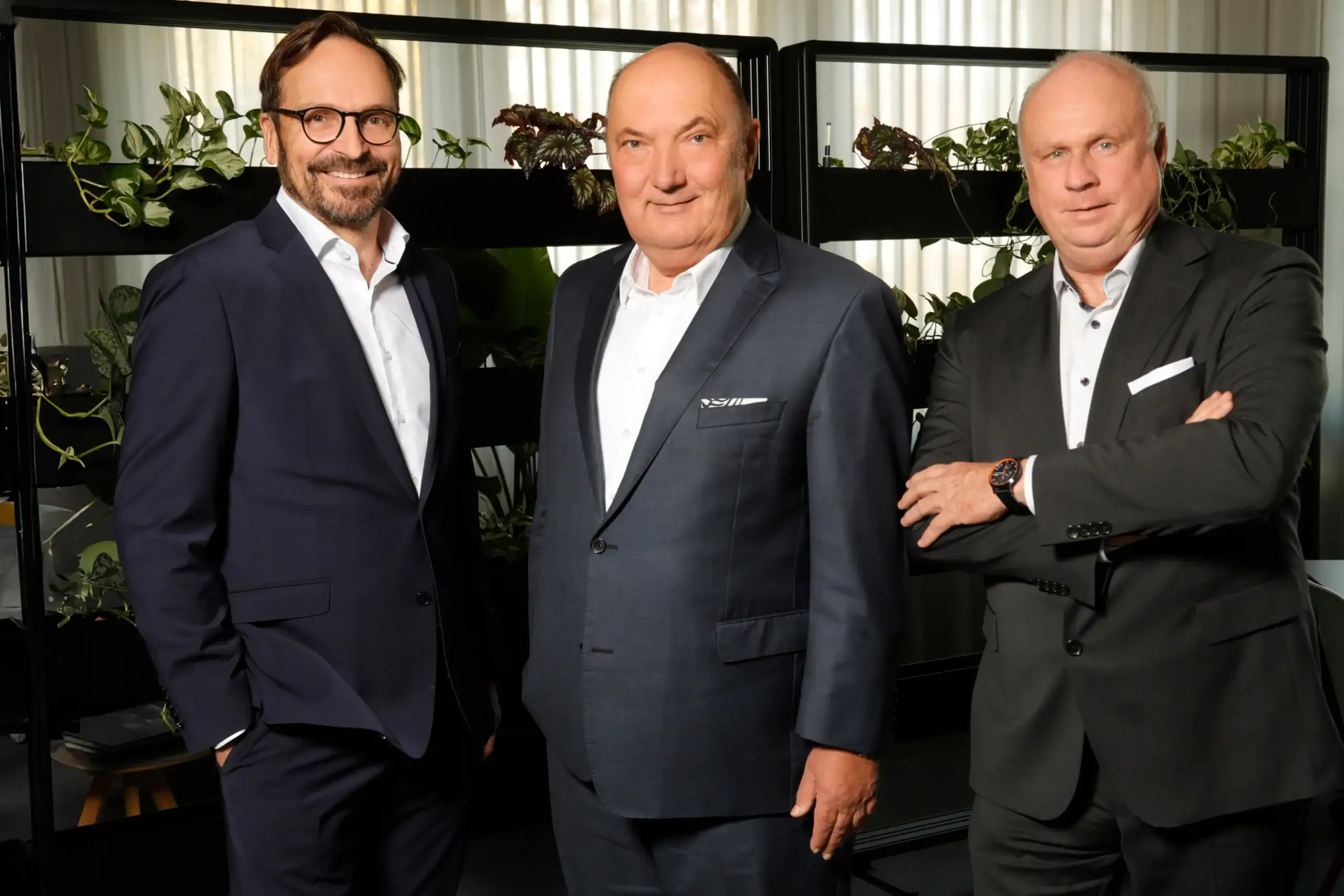 Drei Geschäftsleiter der Wackler Service Group im Business-Outfit vor Pflanzenregal.