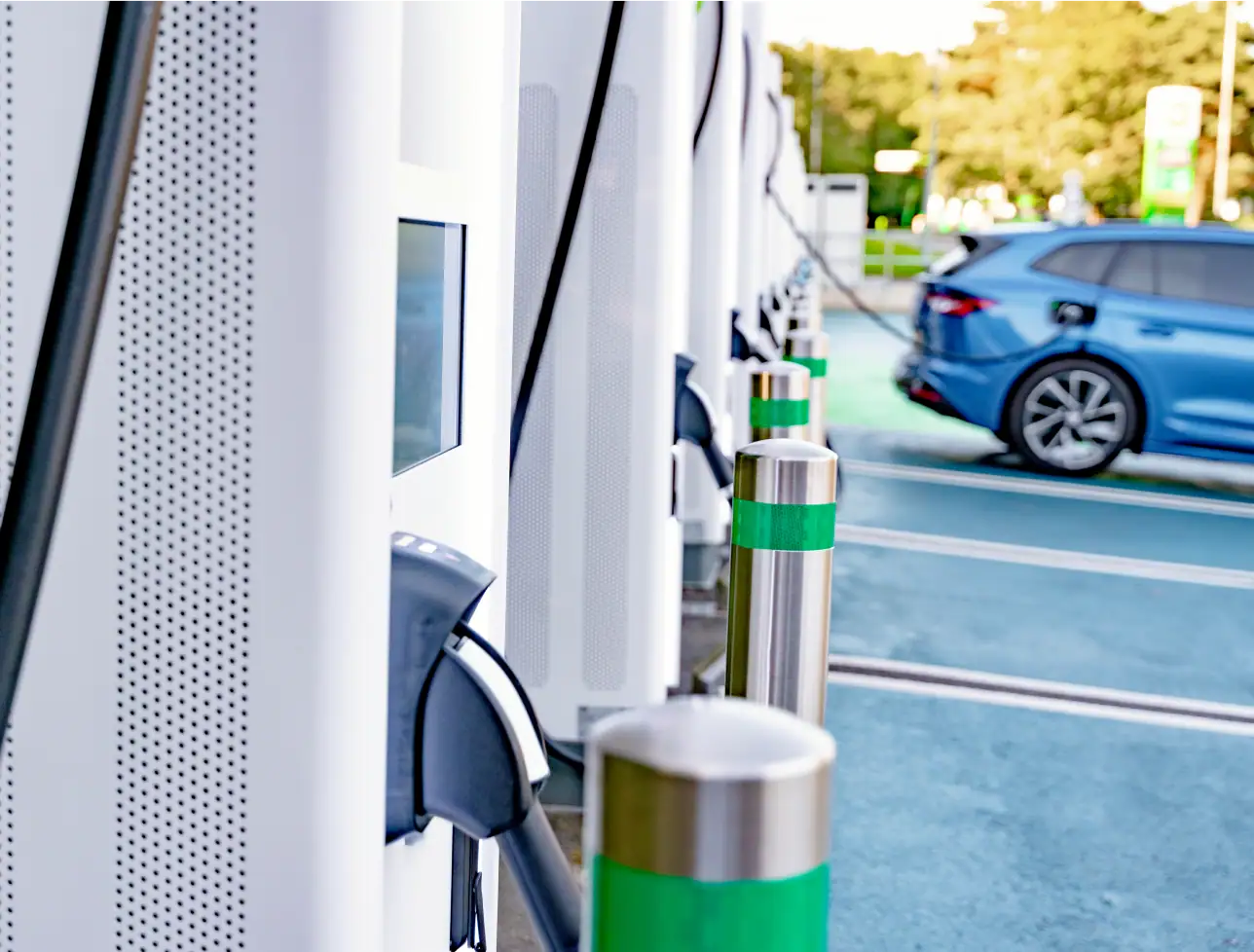 Ladestation für Elektroautos mit Ladekabel und Parkplatz im Hintergrund.