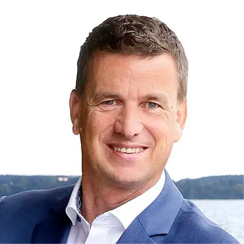 Porträt von Markus Mayr vor Wasser mit Gebäudereinigung im Hintergrund.