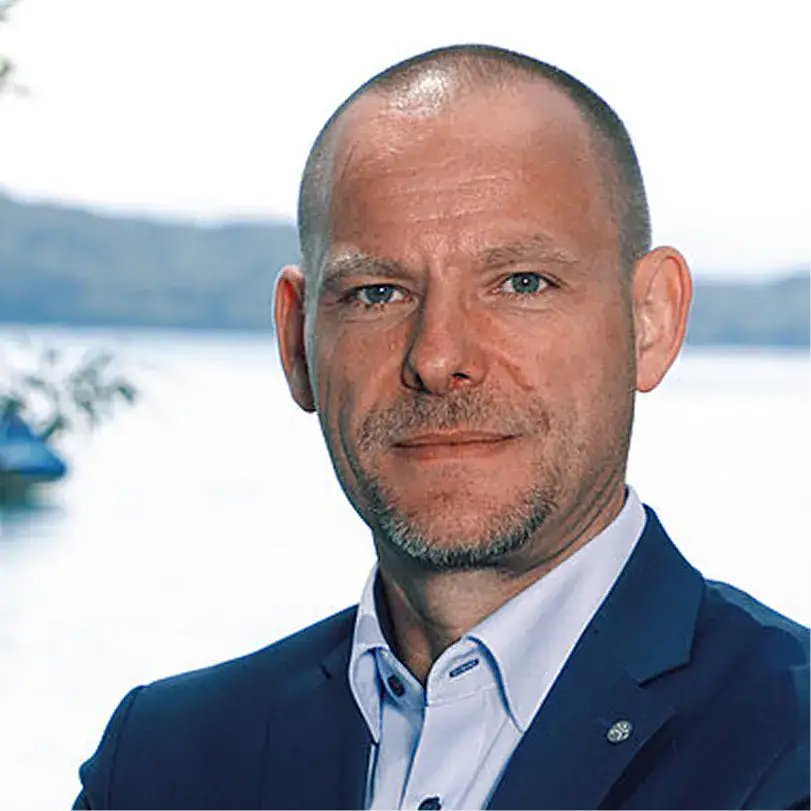 Porträt von Markus Mayr vor Wasser mit Bergen im Hintergrund.