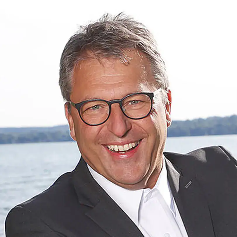 Markus Mayr lächelnd bei Gebäudereinigung im Freien mit Wasser im Hintergrund.
