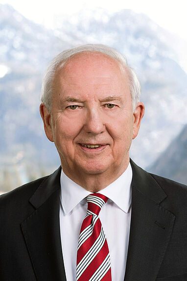 Porträt eines älteren Mannes in Anzug vor Berglandschaft.