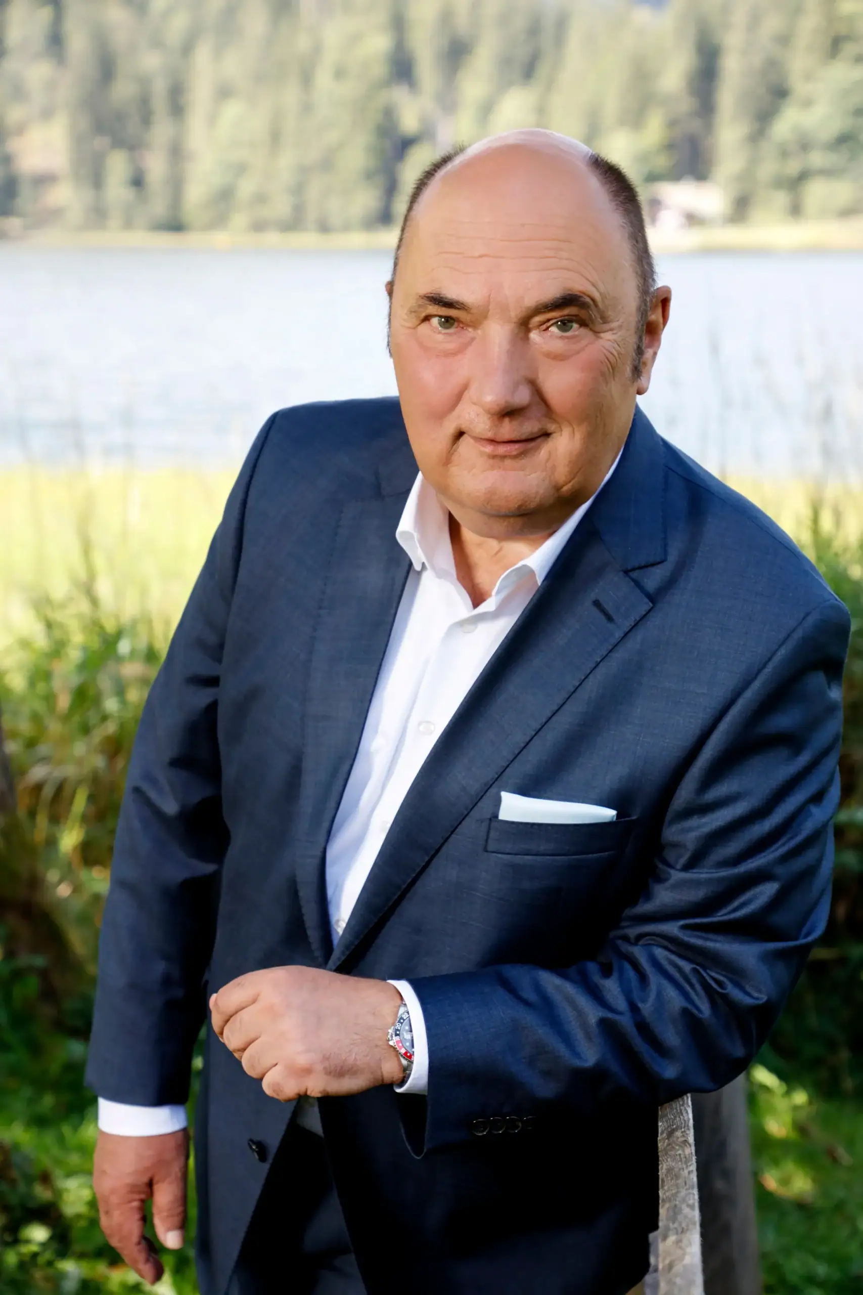 Geschäftsmann in Anzug vor See mit Bäumen im Hintergrund.