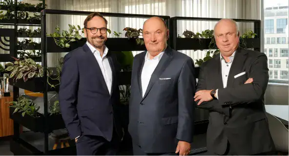 Drei Männer in Businesskleidung vor Pflanzenregal im Büro.