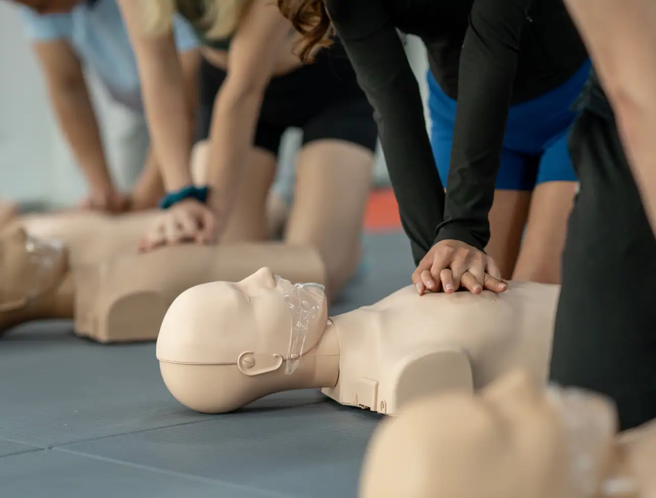 Menschen üben Erste-Hilfe an einer CPR-Puppe in einem Kursraum.
