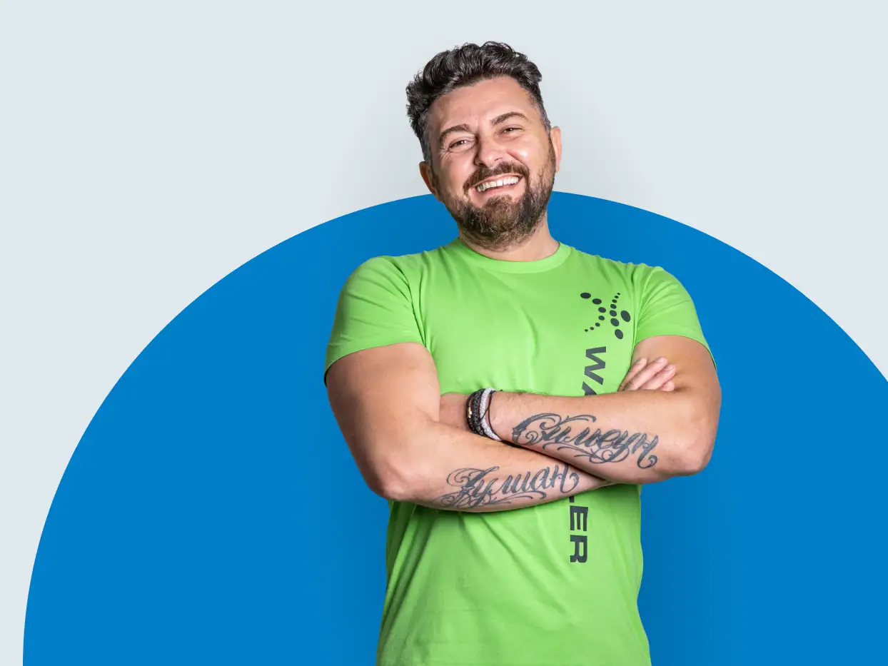 Lächelnder Reinigungsmitarbeiter in grünem T-Shirt vor blauem Hintergrund.