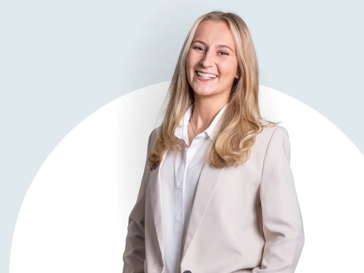 Lächelnde Frau in Businesskleidung vor hellem Hintergrund.