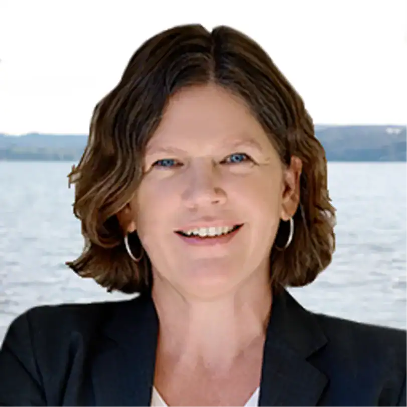 Frau mit dunklem Blazer vor Wasserhintergrund, lächelnd.