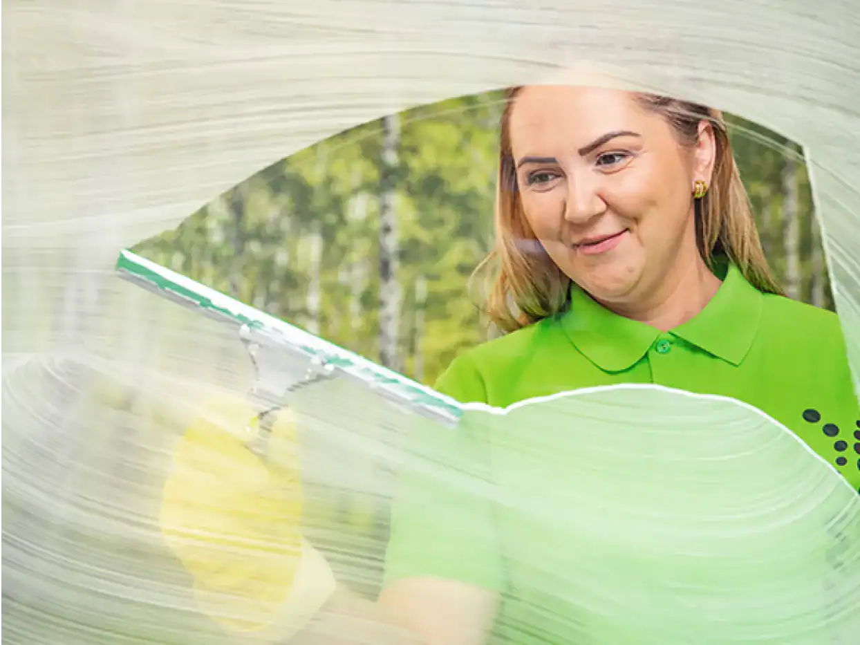 Frau in grüner Uniform bedient Reinigungsroboter im Gebäude.