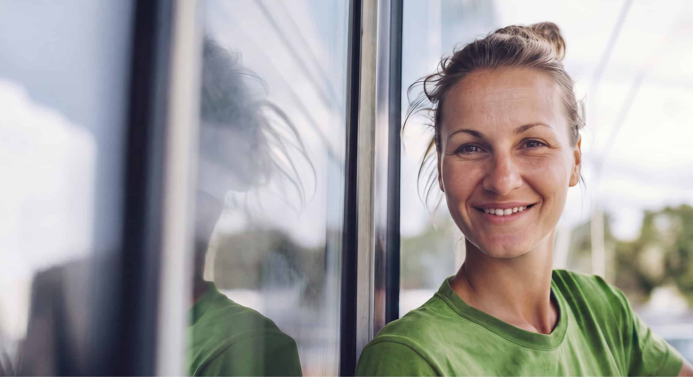 Frau in grüner Arbeitskleidung bei Gebäudereinigung, freundlich und professionell.