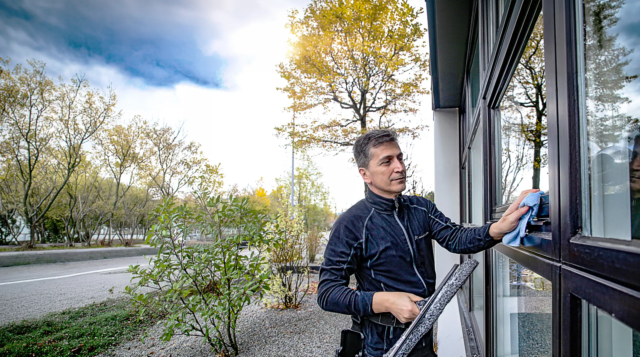 Mann reinigt Fenster mit Reinigungsroboter vor einem modernen Gebäude.