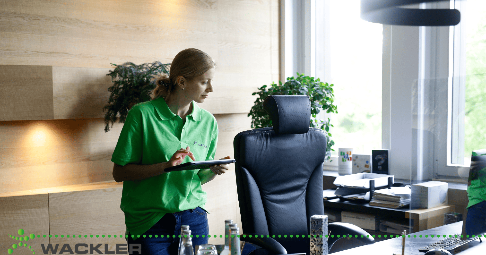 Frau in grüner Arbeitskleidung bei Gebäudereinigung im Büro.