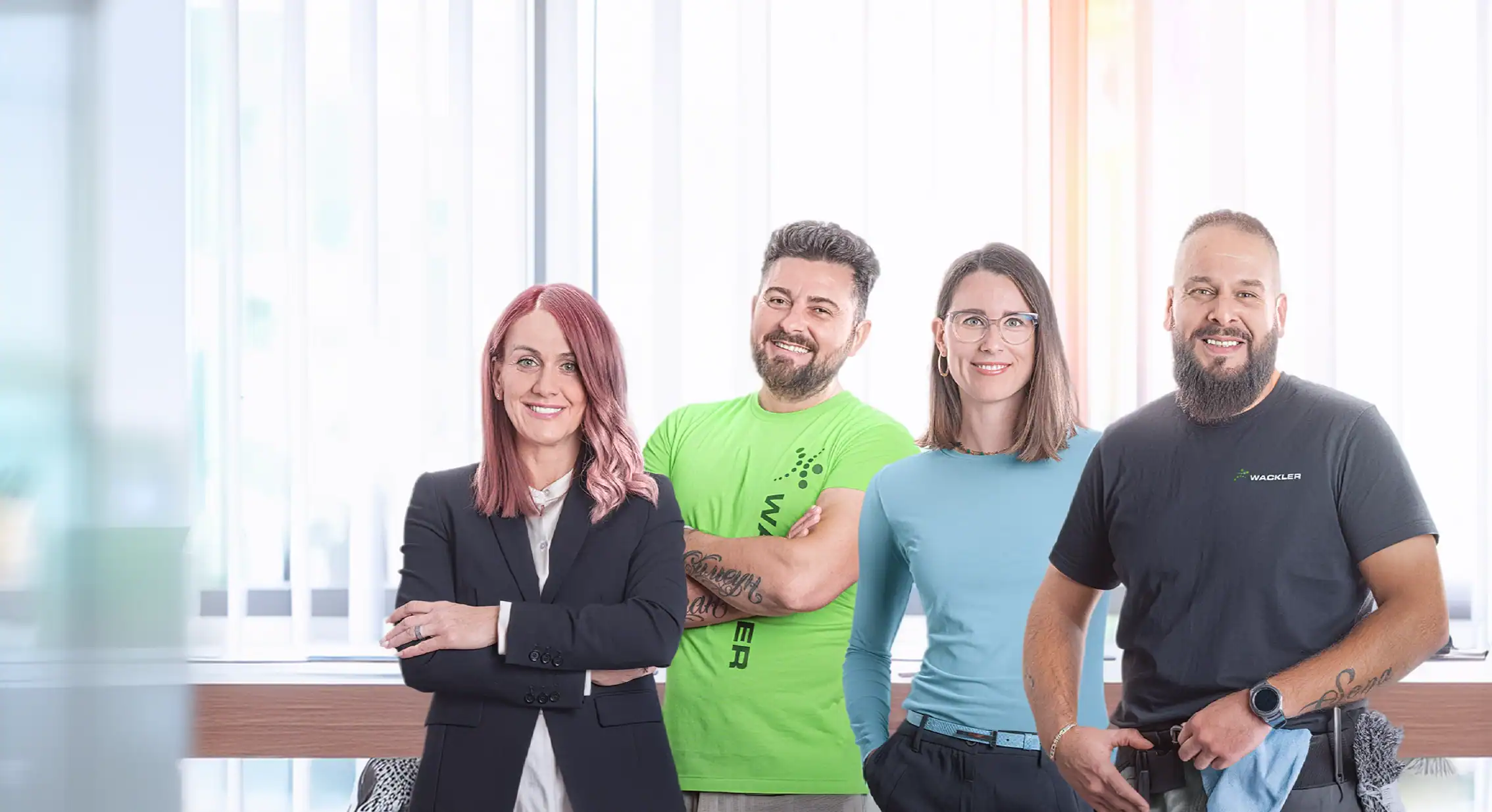 Vier Mitarbeiter der Wackler Service Group im Büro, lächelnd und professionell.
