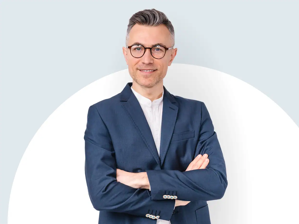 Geschäftsmann in Anzug mit verschränkten Armen vor weißem Hintergrund.