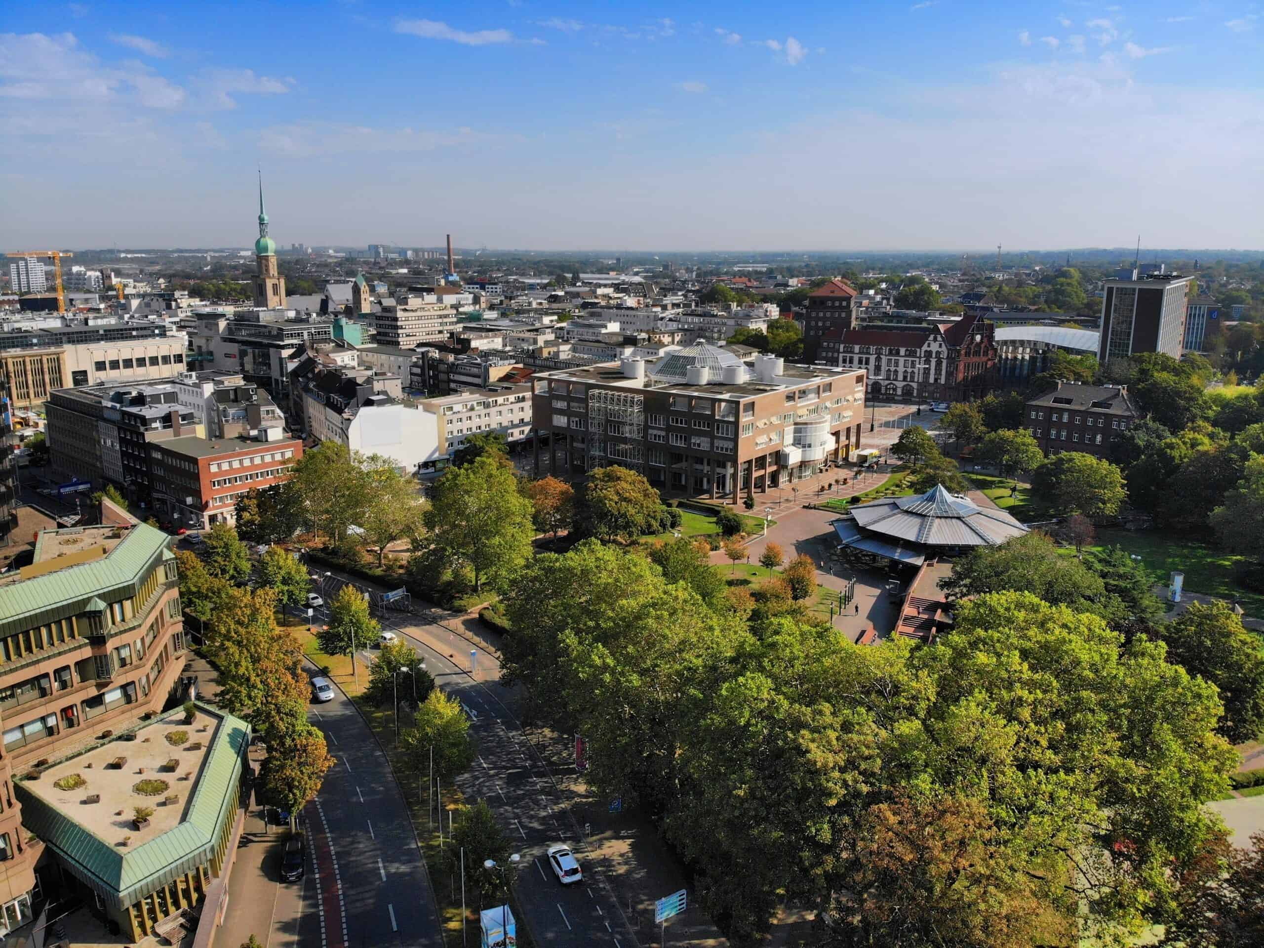 Hochhaus und Stadtpark mit Bäumen und Straßen in einer Großstadt.