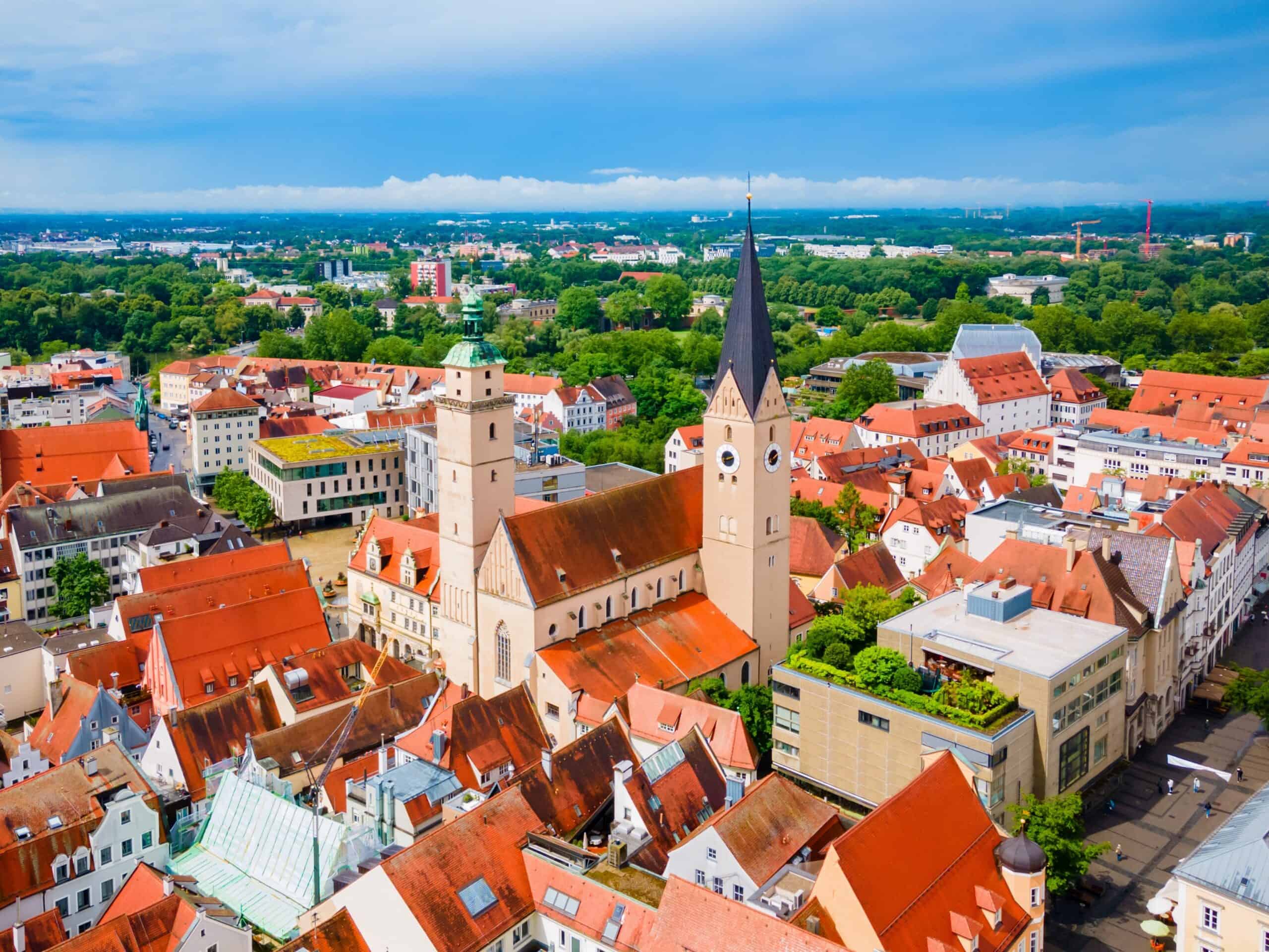 Luftaufnahme einer Stadt mit Kirche und roten Dächern, umgeben von Grünflächen.