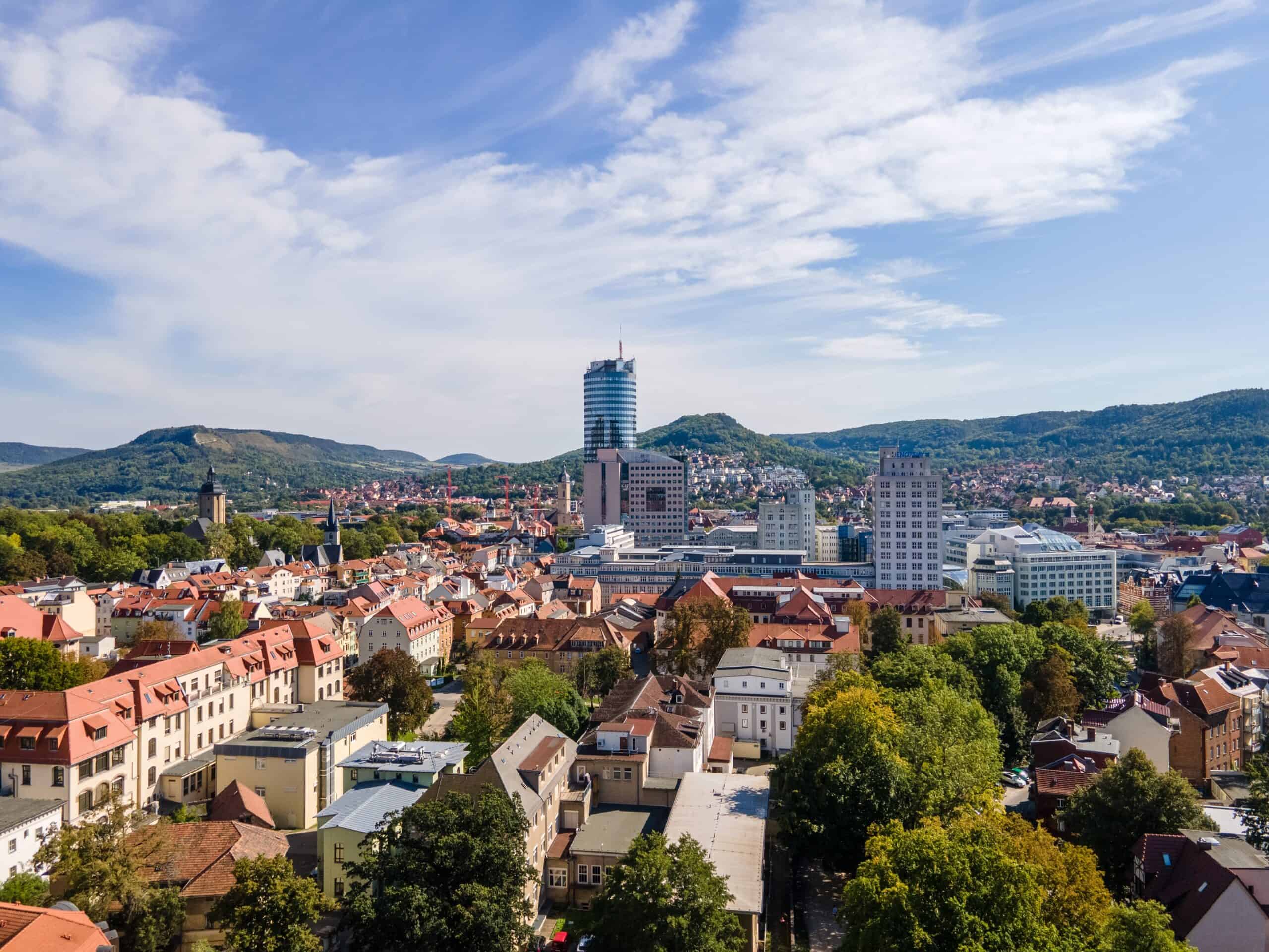 Panorama einer Stadt mit Hochhaus und Bergen im Hintergrund.