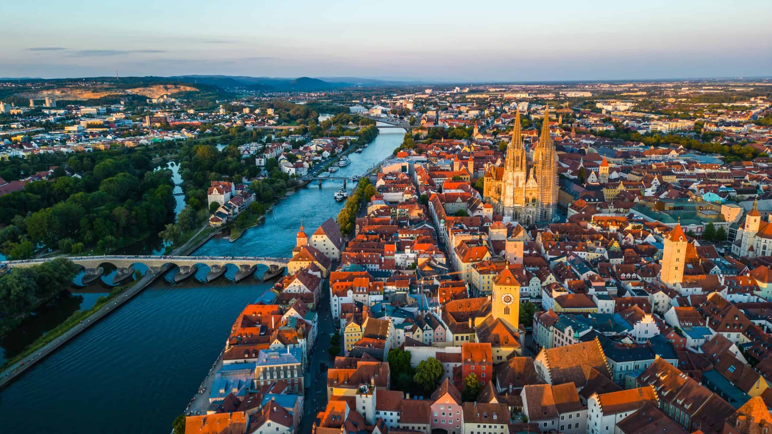 Luftaufnahme einer Stadt mit Fluss, Brücken und historischer Kathedrale bei Sonnenuntergang.